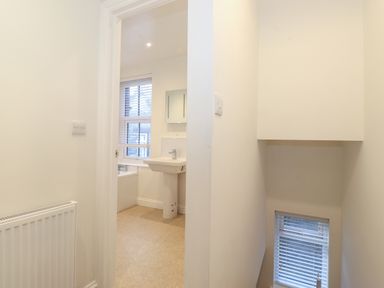 A hallway with a radiator and a doorway leading to a bathroom with a sink and a bathtub and a window with blinds at Jacks Cottage in Keswick
