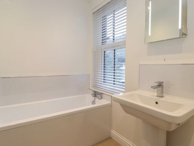 A bathroom with a bathtub a window with blinds and a wall-mounted sink with a mirror above at Jacks Cottage in Keswick