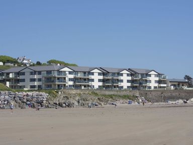 A beachfront modern apartment complex with balconies near a sandy beach with people at 19 Burgh Island Causeway in Bigbury-On-Sea