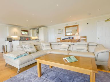 A living room with a beige sectional sofa a wooden coffee table and a kitchen area in the background at 19 Burgh Island Causeway in Bigbury-On-Sea