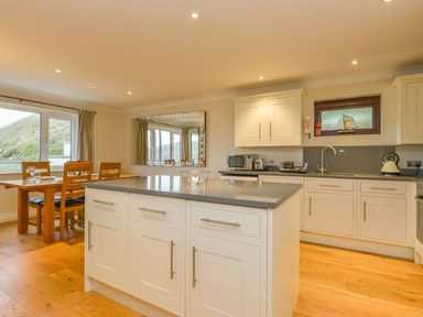 A kitchen with an island countertop and dining table with chairs at 19 Burgh Island Causeway in Bigbury-On-Sea