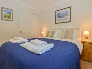 A bedroom with a bed with folded towels on a blue bedspread and framed pictures on the walls at 19 Burgh Island Causeway in Bigbury-On-Sea