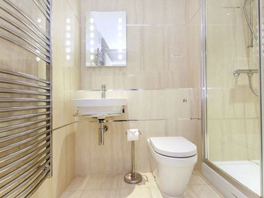 A bathroom with a wall-mounted sink, toilet, glass shower enclosure, and a metal towel radiator at 19 Burgh Island Causeway in Bigbury-On-Sea