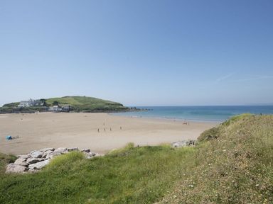 A sandy beach with a few people walking near the water and grassy hills with buildings in the background at 19 Burgh Island Causeway in Bigbury-On-Sea
