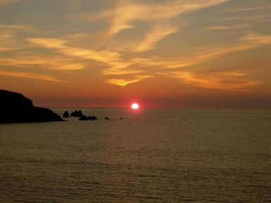 A sunset over the ocean with rocky cliffs on the left at 19 Burgh Island Causeway in Bigbury-On-Sea