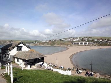 A beach with people sitting near a building and houses on a hill at 19 Burgh Island Causeway in Bigbury-On-Sea