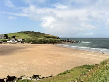 A wide sandy beach with a few people walking near the water and green hills with houses in the background at 19 Burgh Island Causeway in Bigbury-On-Sea