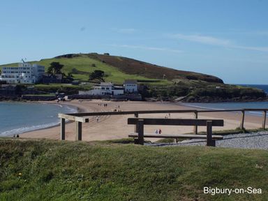 A beach with people walking near buildings and a hill at Bigbury-On-Sea