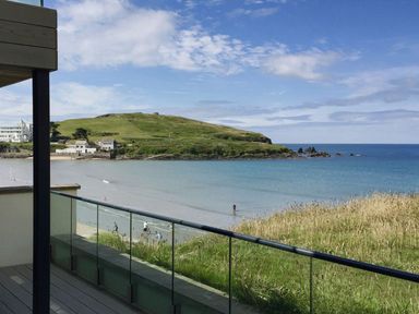A balcony with glass railing overlooking a beach green hill and ocean at 19 Burgh Island Causeway in Bigbury-On-Sea