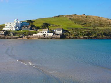 A coastal scene with buildings along the shore and a grassy hill behind at 19 Burgh Island Causeway Bigbury-On-Sea