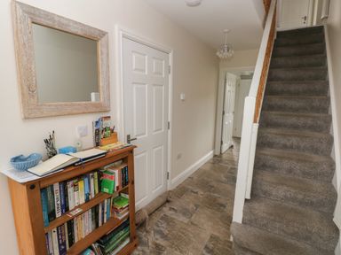 A hallway with a carpeted staircase a bookshelf a mirror and closed doors at Llygad Y Lleuad Moon in Burry Port