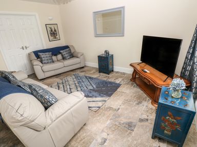 A living room with two beige sofas a TV on a wooden stand a blue side table and a blue patterned rug at Llygad Y Lleuad Moon in Burry Port