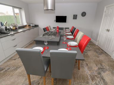 A kitchen with a long dining table and chairs in red black grey and cream with a built in gas stove and kitchen cabinets at Llygad Y Lleuad Moon in Burry Port