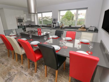 A kitchen with a long dining table with multicolored chairs set with plates and glasses at Llygad Y Lleuad Moon in Burry Port