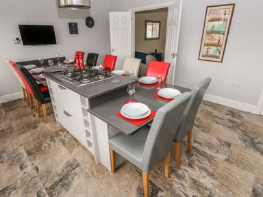 A dining area with a kitchen island and stovetop surrounded by chairs in a room at Llygad Y Lleuad Moon in Burry Port