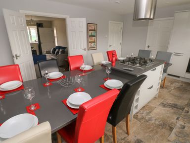 A kitchen with a large dining table set with plates and glasses and a stove on an island unit at Llygad Y Lleuad ( Moon) in Burry Port