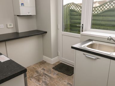 A kitchen with a stainless steel sink a black countertop a white door and a window at Llygad Y Lleuad  Moon in Burry Port