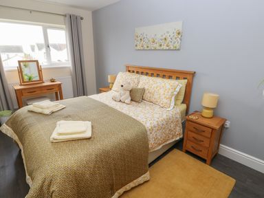 A bedroom with a bed a bedside table with a lamp a dressing table and a window at Llygad Y Lleuad Moon in Burry Port