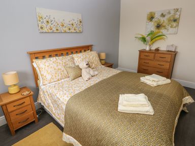 A bedroom with a double bed with floral bedding a teddy bear on the bed and wooden furniture at Llygad Y Lleuad ( Moon) in Burry Port