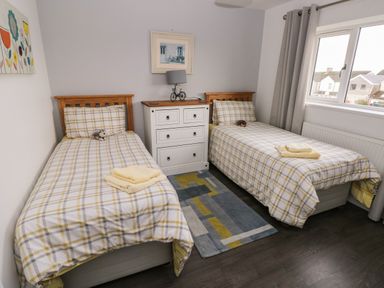 A bedroom with two single beds a white dresser and a window with curtains at Llygad Y Lleuad ( Moon) in Burry Port