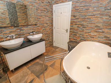 A bathroom with two sinks a freestanding bathtub and a laundry basket at Llygad Y Lleuad Moon in Burry Port