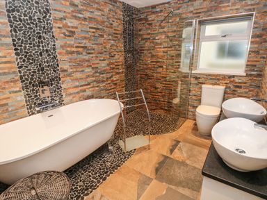 A bathroom with a bathtub, walk-in shower, toilet, two sinks, and stone tile walls at Llygad Y Lleuad ( Moon) in Burry Port