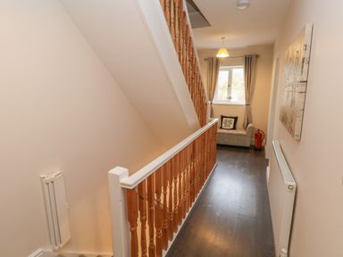 A hallway with wooden staircase railing a small cushioned bench with a pillow and a fire extinguisher near a window at Llygad Y Lleuad Moon in Burry Port