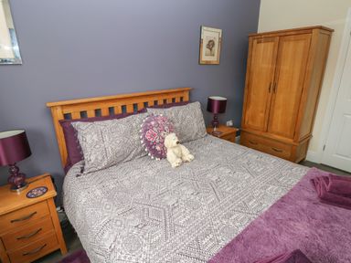 A bedroom with a wooden bed with patterned bedding and a teddy bear on the bed at Llygad Y Lleuad ( Moon) in Burry Port