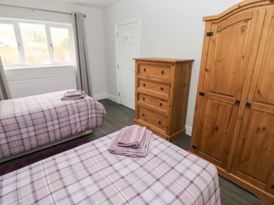 A bedroom with two single beds with plaid bedspreads a wooden chest of drawers and a wooden wardrobe at Llygad Y Lleuad ( Moon) in Burry Port
