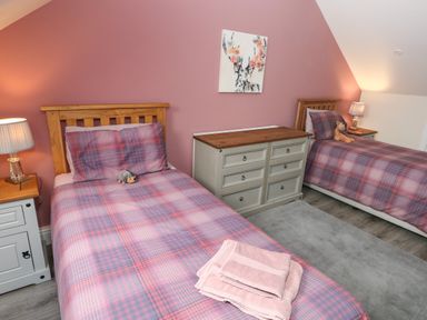 A bedroom with two single beds side by side with plaid bedding and wooden headboards at Llygad Y Lleuad Moon in Burry Port