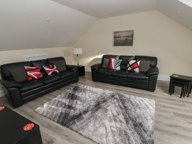 A living room with two black leather sofas with cushions a floor lamp a gray patterned rug wooden flooring and a framed picture on the wall at Llygad Y Lleuad Moon in Burry Port
