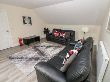 A living room with two black leather sofas and a patterned rug at Llygad Y Lleuad ( Moon) in Burry Port