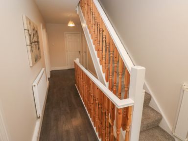 A hallway with wooden staircase and carpeted stairs a radiator and a door at Llygad Y Lleuad ( Moon) in Burry Port