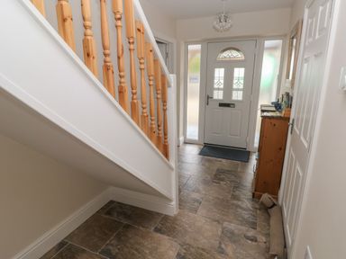 An entryway with a staircase railing on the left a front door with frosted windows a wooden cabinet with items on top and a draft stopper on the floor at Llygad Y Lleuad Moon Burry Port