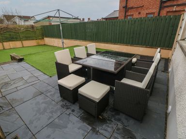 Outdoor patio area with dining table and chairs on stone tiles next to an artificial grass lawn at Llygad Y Lleuad Moon in Burry Port