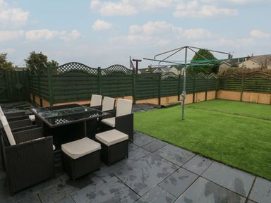 A backyard with a patio dining set and a rotary clothesline on artificial grass at Llygad Y Lleuad Moon in Burry Port