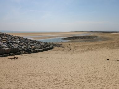 A sandy beach with a rocky embankment and water inlet at Llygad Y Lleuad ( Moon) in Burry Port