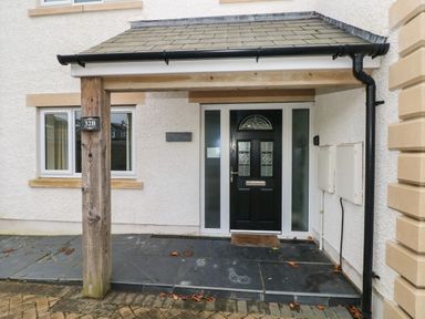 The entrance of a house with a black front door under a small roof supported by wooden posts at Llygad Yr Haul Sun in Burry Port