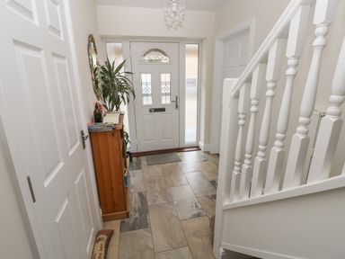 A hallway with a front door a wooden cabinet a plant a mirror and white staircase at Llygad Yr Haul Sun in Burry Port