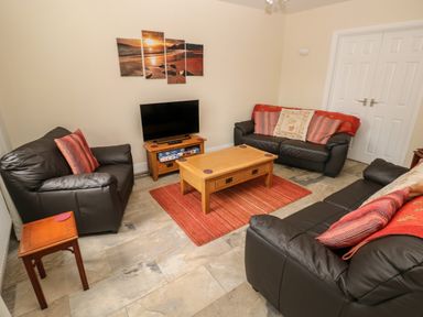 A living room with three black leather sofas a wooden coffee table and a television on a wooden stand at Llygad Yr Haul Sun in Burry Port
