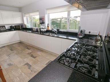 A kitchen with black countertops white cabinets gas stove and windows showing a garden at Llygad Yr Haul Sun in Burry Port