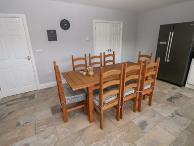 A dining area with a wooden table and eight wooden chairs with cushions in a kitchen at Llygad Yr Haul Sun in Burry Port