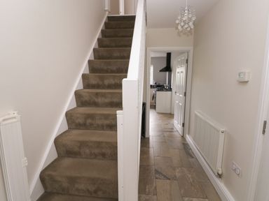A hallway with carpeted stairs and a tiled floor leading to a kitchen at Llygad Yr Haul in Burry Port
