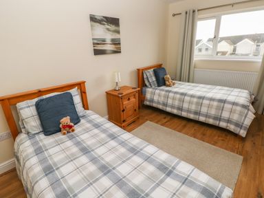 A bedroom with two single beds with plaid bedding a wooden nightstand a lamp and teddy bears at Llygad Yr Haul Sun in Burry Port