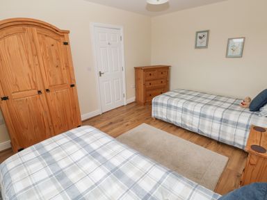 A bedroom with two single beds covered with plaid bedspreads a wooden wardrobe a chest of drawers and two framed pictures on the wall at Llygad Yr Haul Sun in Burry Port