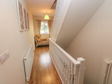 A hallway with wooden floor radiator and a small sofa with teddy bear under a window at Llygad Yr Haul Sun in Burry Port
