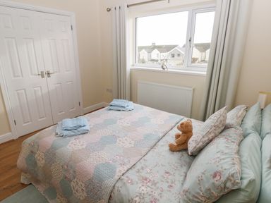A bedroom with a double bed with floral bedding and a teddy bear near a window with folded towels on the bed at Llygad Yr Haul Sun in Burry Port