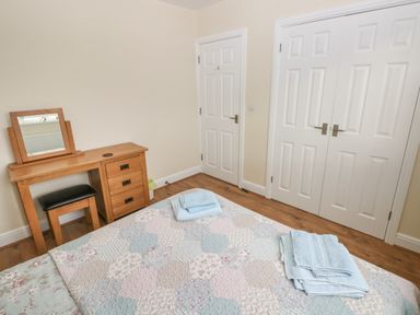 A bedroom with a wooden vanity table with mirror and stool a bed with folded towels a door and a double closet at Llygad Yr Haul Sun in Burry Port