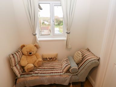 A small room with a chaise lounge and a teddy bear near a window at Llygad Yr Haul Sun in Burry Port