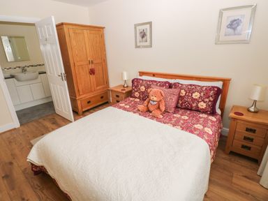 A bedroom with a wooden bed red floral bedding a teddy bear wooden wardrobe and bedside tables with lamps at Llygad Yr Haul Sun in Burry Port
